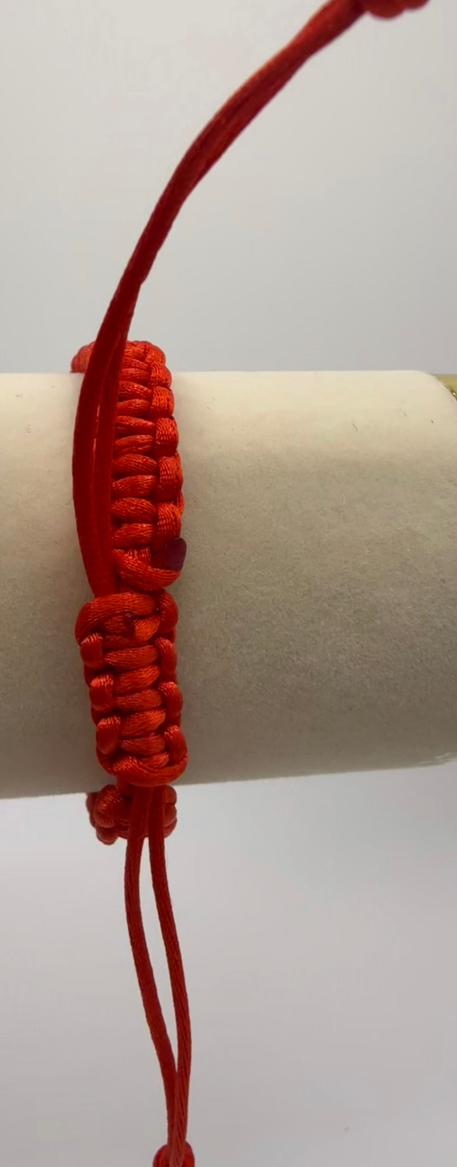 Red bracelet on a cylindrical white object with gold band against a light gray background