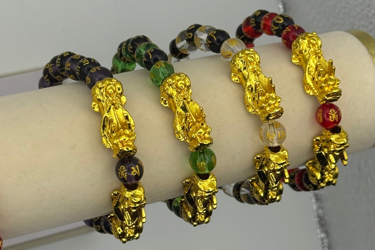Bracelets with gold figures and colorful beads on a wrist against a neutral background